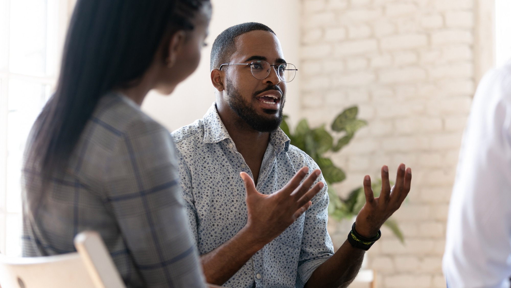 A man passionately discusses ideas during a conversation, seated in a bright, airy space. His gestures emphasize key points to an engaged audience.