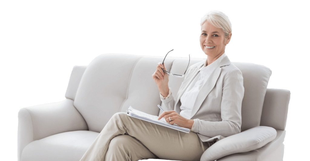 Professional woman in a light suit sits on a white couch, smiling while holding glasses and reviewing documents, suggesting a collaborative or advisory context.